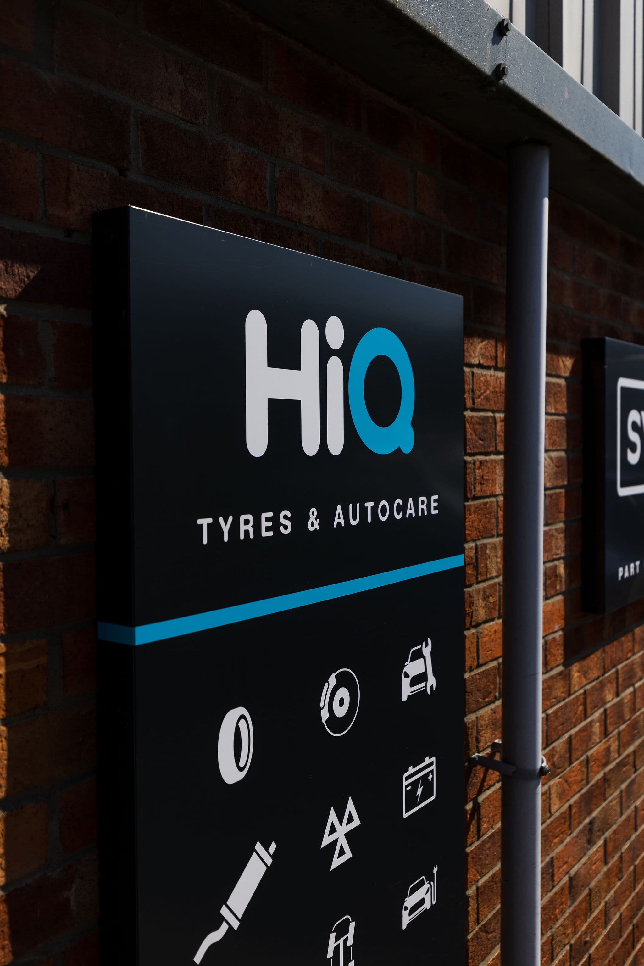 HiQ Tyres & Autocare sign with service icons, including an exhaust