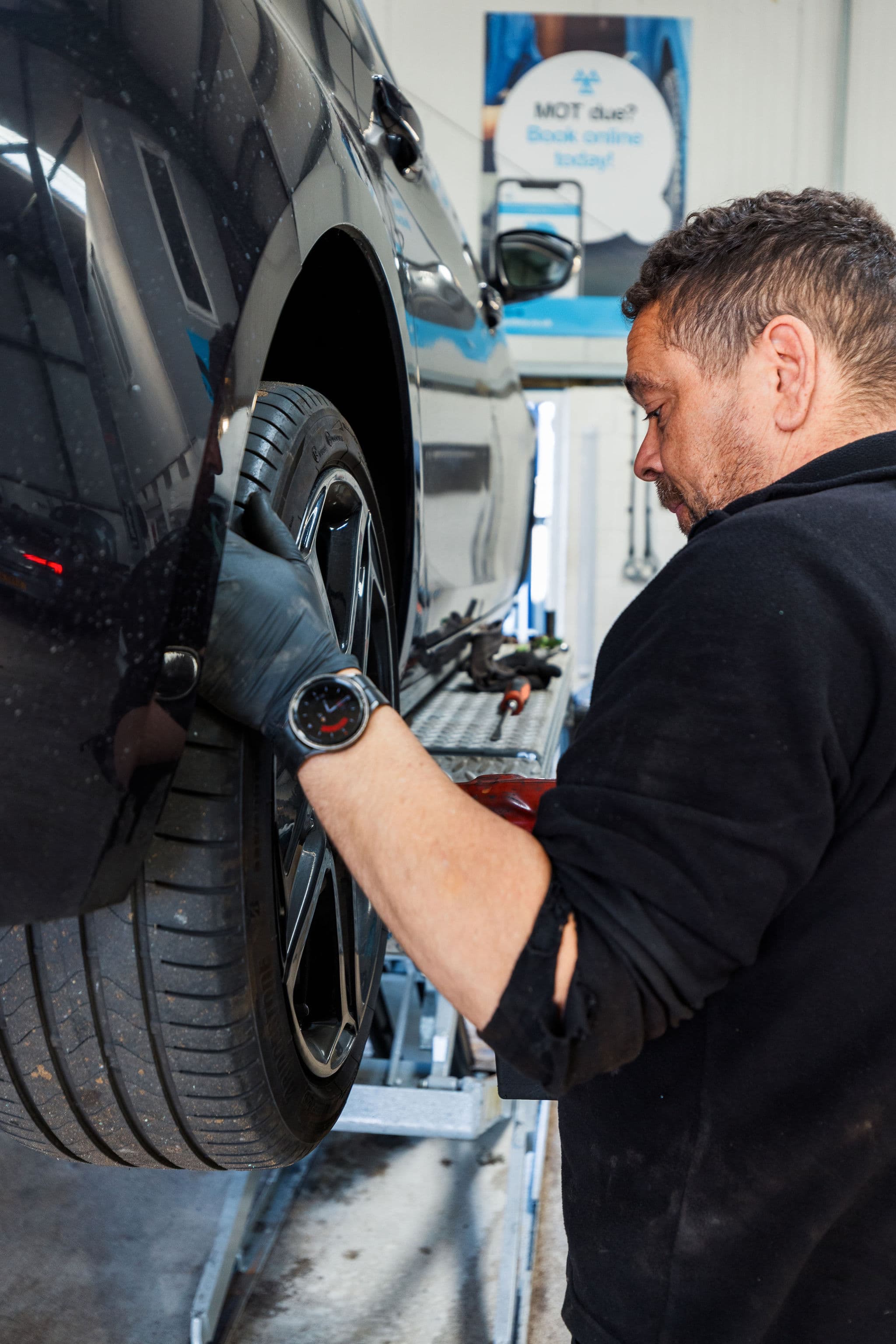 Synergy technician working on a wheel of a car raised on a ramp